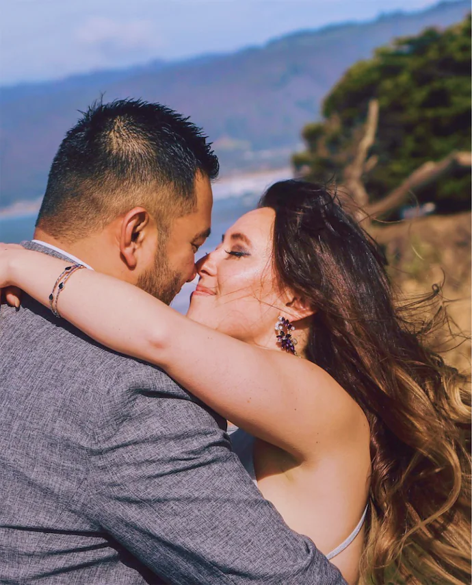 The middle-aged couple is hugging each other on the cliff edge. They have a great relationship.