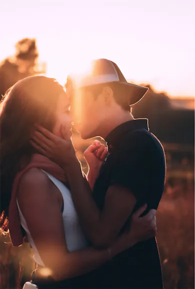 Young couple having their first date kiss in a field during a sunset.
